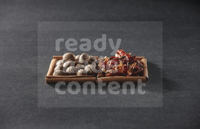 2 squares of cinnamon sticks full of nutmegs and dried red chilis on black flooring