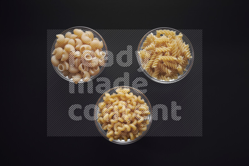 Different pasta types in glass bowls on black background