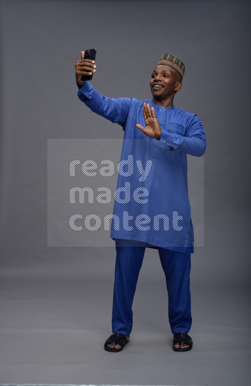 Man wearing Nigerian outfit standing taking selfie on gray background