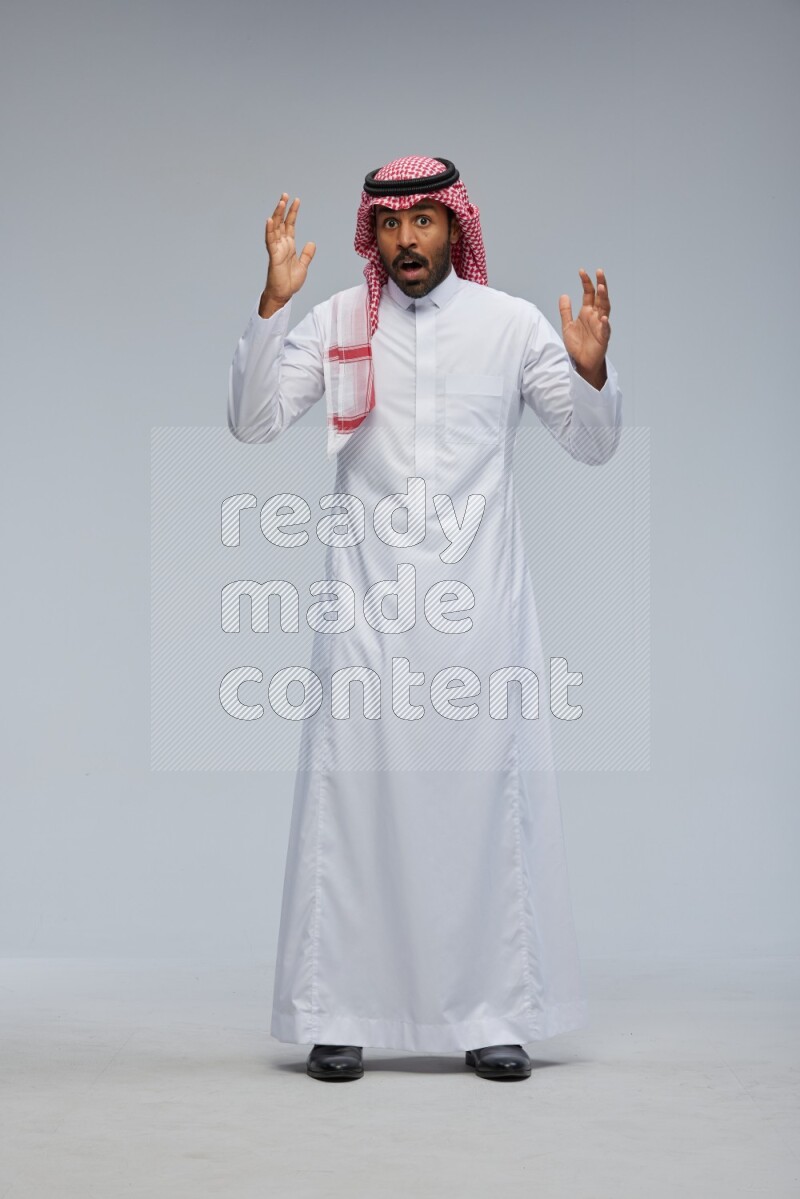 Saudi man Wearing Thob and shomag standing interacting with the camera on Gray background