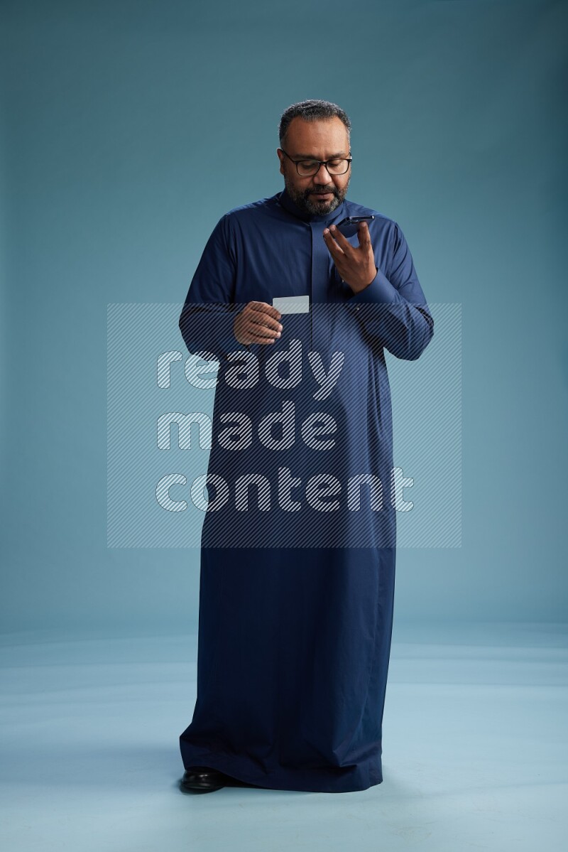 Saudi Man without shimag Standing holding ATM while talking on phone on blue background