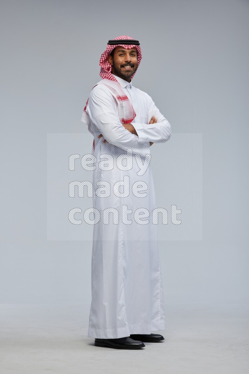 Saudi man Wearing Thob and shomag standing with crossed arms on Gray background