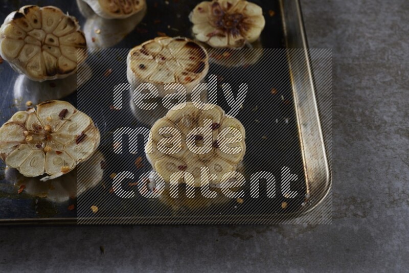 half's roasted garlic in a stainless tray on a grey textured countertop