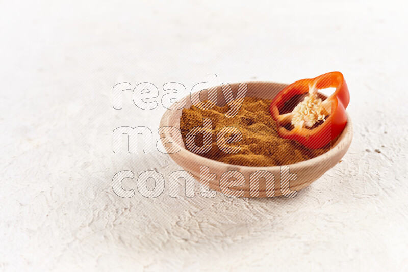 A wooden bowl full of ground paprika powder on white background