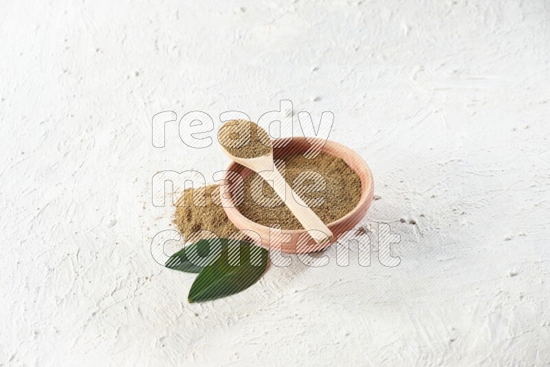 A wooden bowl and wooden spoon full of cumin powder on textured white flooring