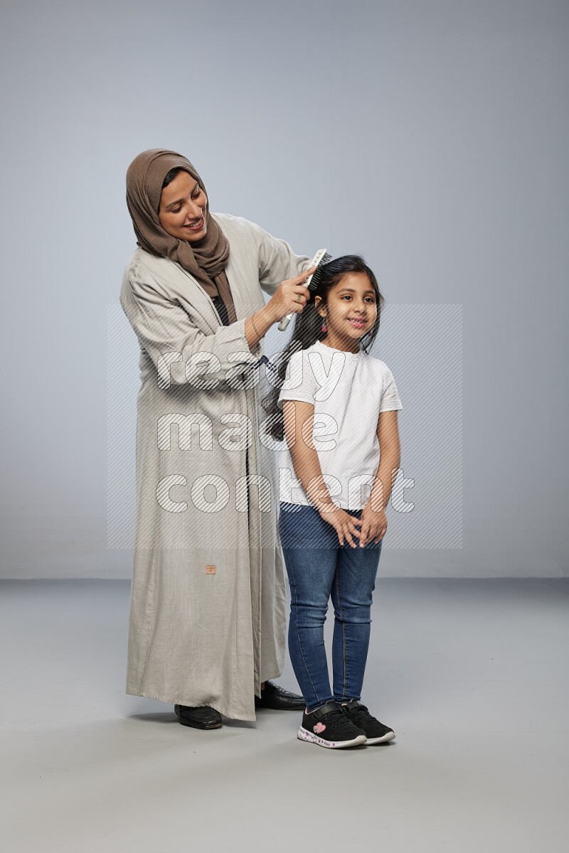 Mom standing styling hair for her daughter on gray background