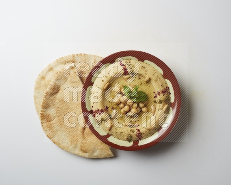 Hummus in a traditional plate garnished with zaatar & sumak on a white background