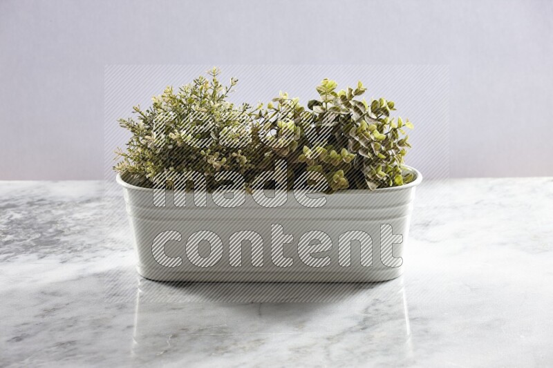 Multiple green artificial plants in white pot on grey marble background