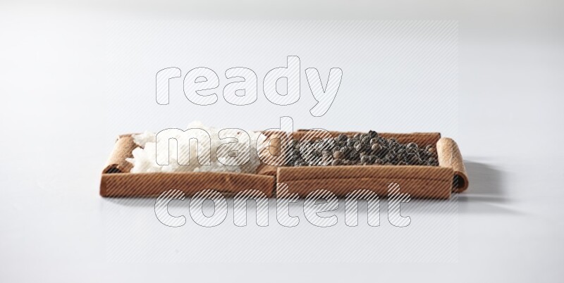 مربعان من أعواد القرفة ممتلئان بحبوب الفلفل الأسود والملح الأبيض علي خلفية بيضاء