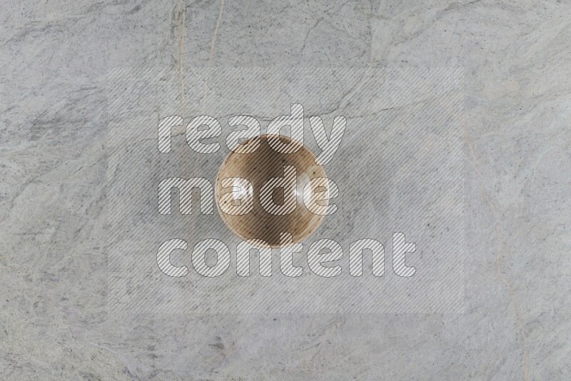 A small beige pottery bowl on grey marble background