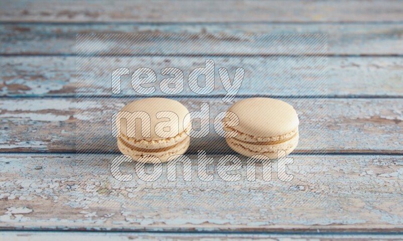 45º Shot of two White Caramel fleur de sel macarons on a light blue wooden background