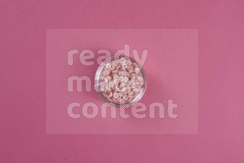 Pink buttons in a glass bowl on pink background