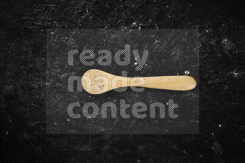 A wooden spoon full of ground ginger powder on black background