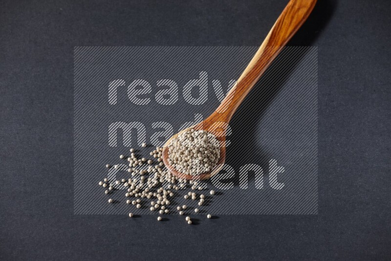 A wooden ladle full of white pepper beads on black flooring