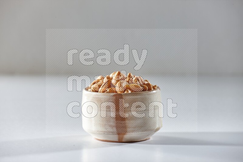 A beige ceramic bowl full of cashews on a white background in different angles