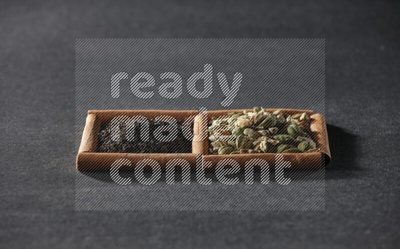 2 squares of cinnamon sticks full of cardamom and black tea on black flooring