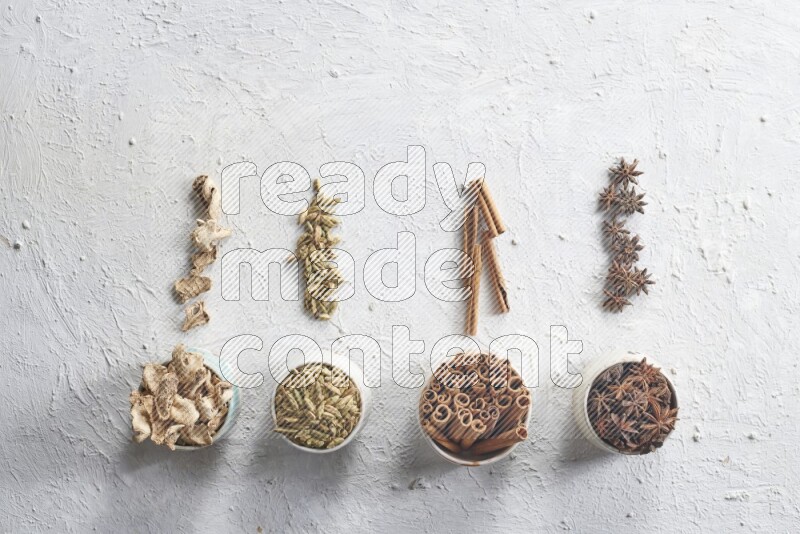 Cardamom, ginger, cinnamon sticks and star anise in 4 bowls on a textured white background