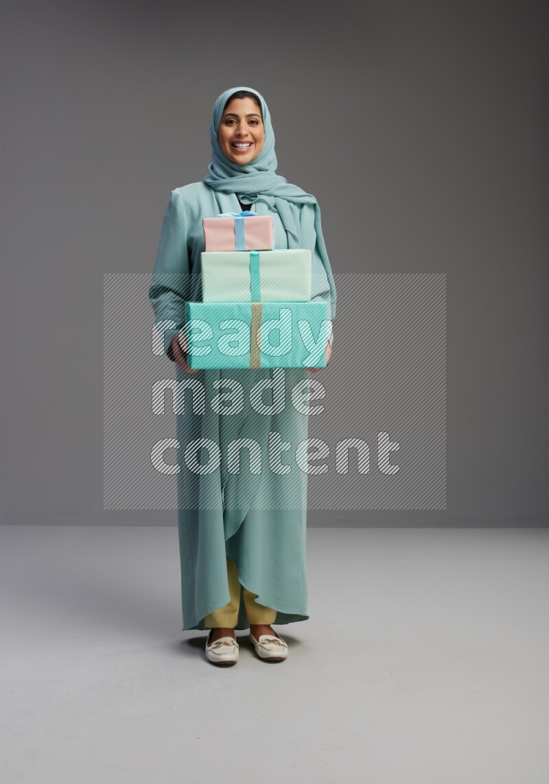 Saudi Woman wearing Abaya standing holding gift box on Gray background