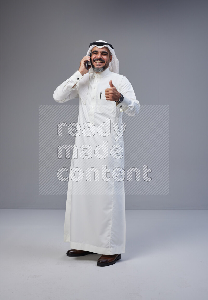 Saudi man Wearing Thob and white Shomag standing talking on phone on Gray background