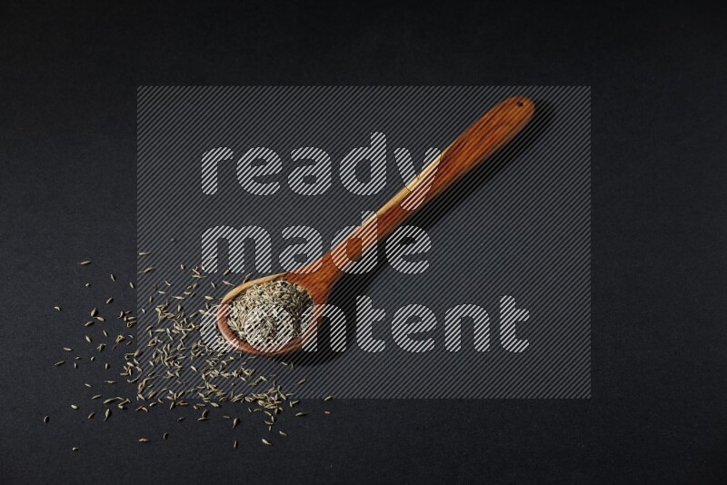 A wooden ladle full of cumin seeds on black flooring