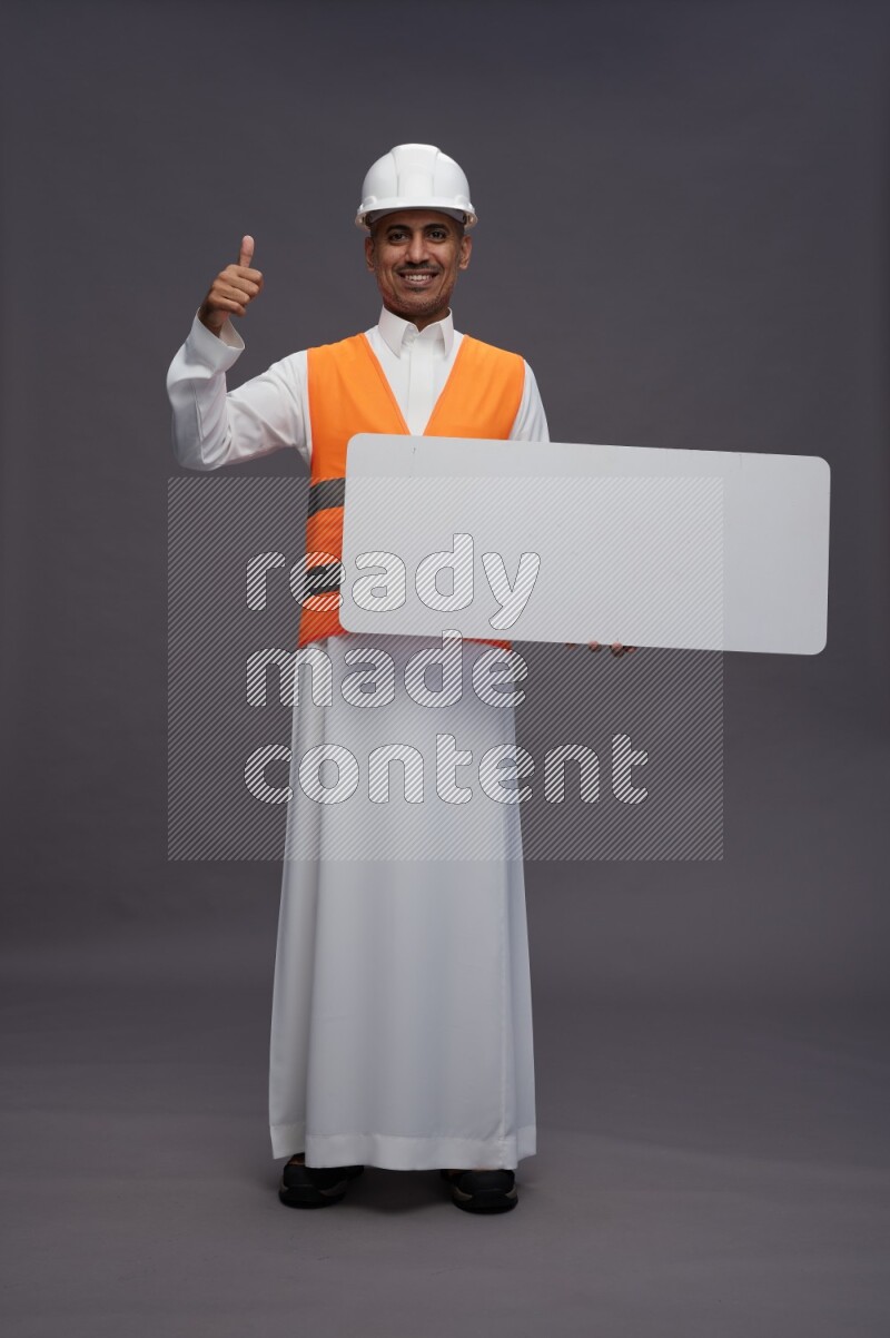 Saudi man wearing thob with engineer vest standing holding board on gray background