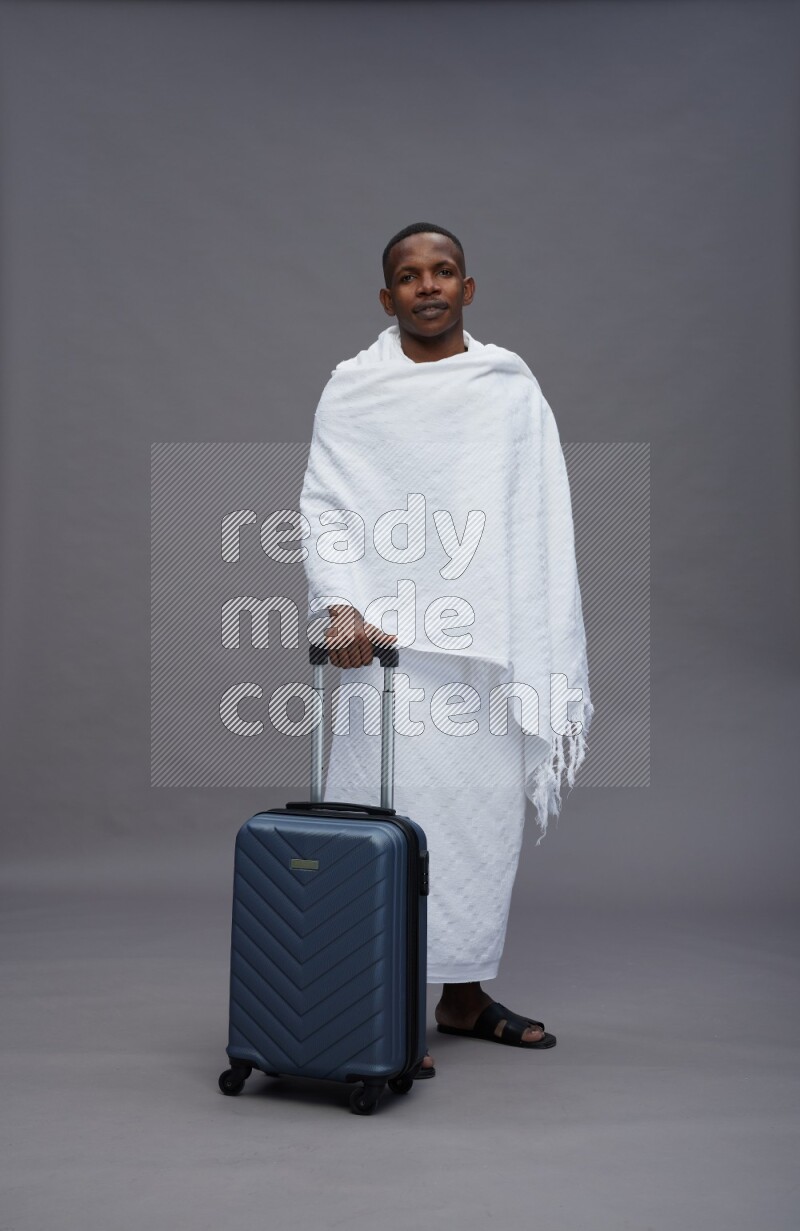 A man wearing Ehram Standing holding traveling bag on gray background