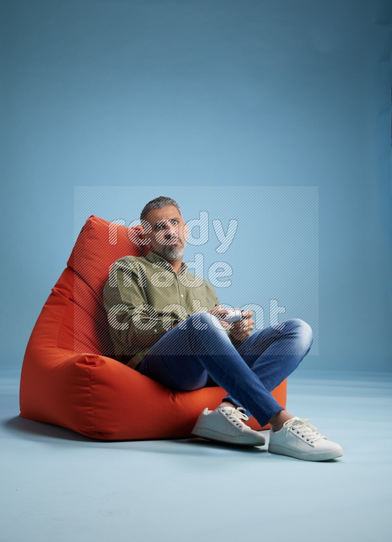 A man sitting on an orange beanbag and gaming with joystick