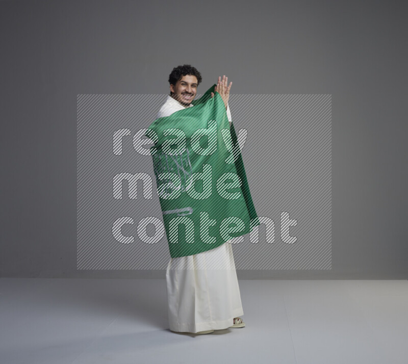 رجل سعودي يرتدي ثوب ابيض ويحمل علم السعودية