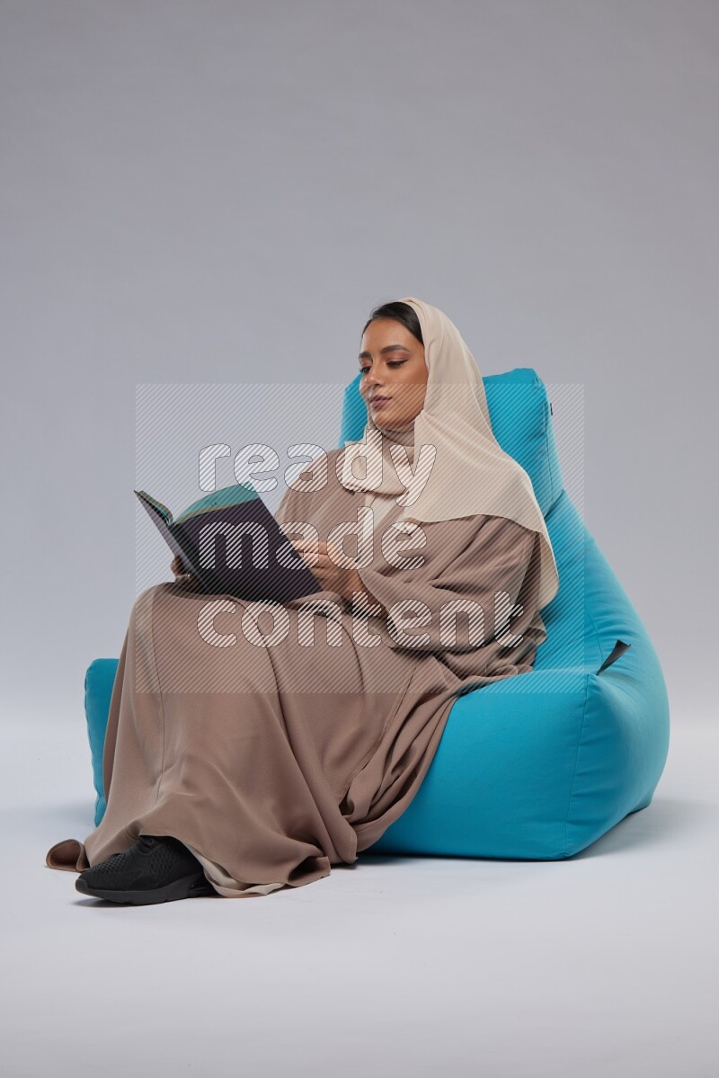 A Saudi woman sitting on a blue beanbag and drinking coffee