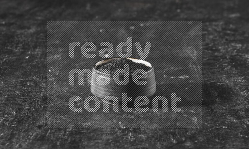 A black pottery bowl full of black seeds on a textured black flooring
