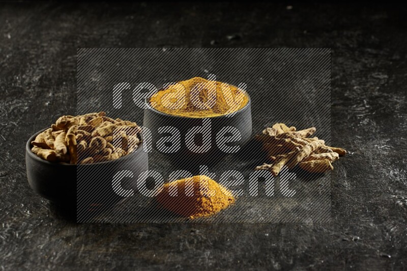 وعاءان من الفخار باللون الأسود، أحدهما ممتلئ ببودرة الكركم والآخر ممتلئ بأصابع كاملة من الكركم المجفف على خلفية سوداء