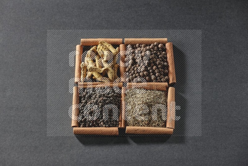 4 squares of cinnamon sticks full of black pepper, cumin, allspice and turmeric fingers on black flooring