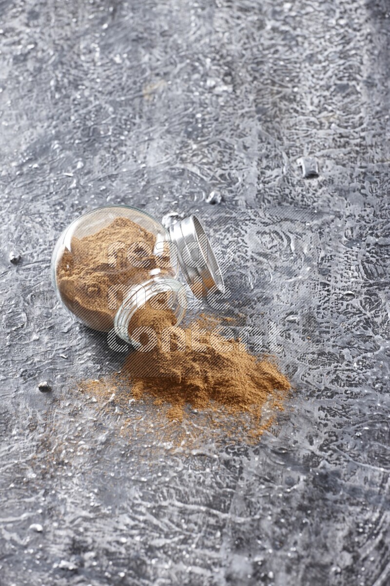 Flipped herbal glass jar full of cinnamon powder on textured black background