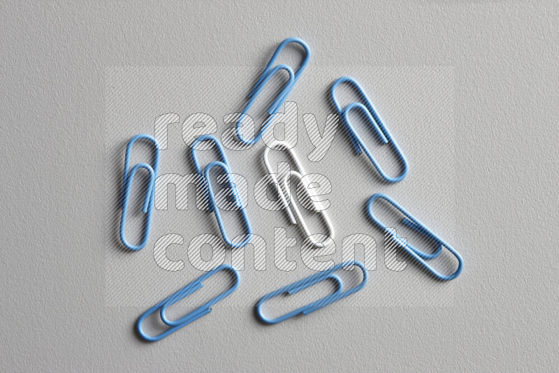 A bunch of blue paper clips with a different colored paper clip in the center on grey background