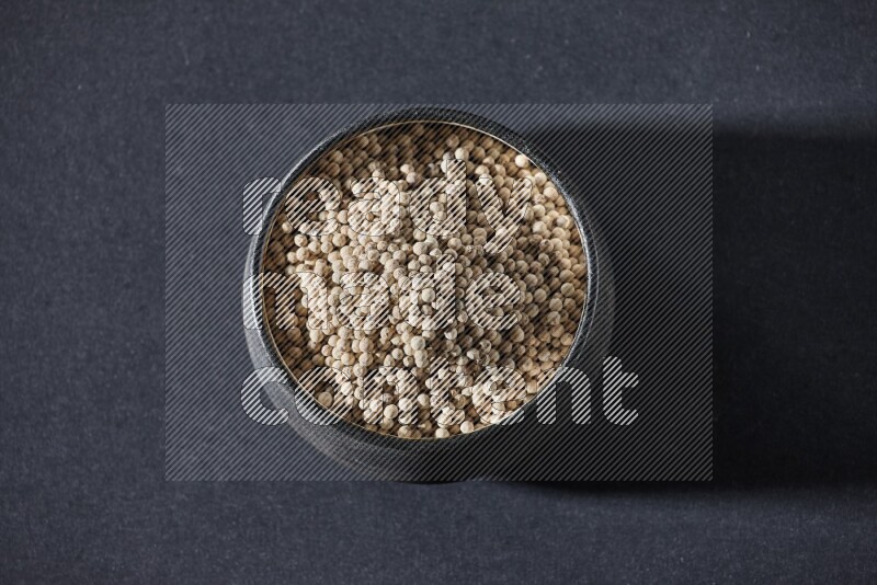 Black pottery bowl full of white pepper on black flooring