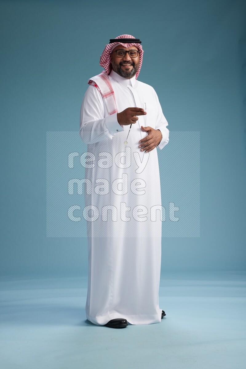 Saudi Man with shimag Standing Interacting with the camera on blue background