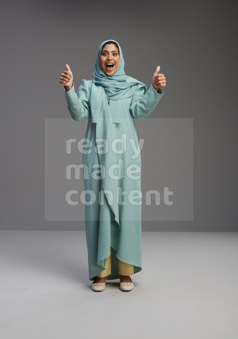 Saudi Woman wearing Abaya standing interacting with the camera on Gray background