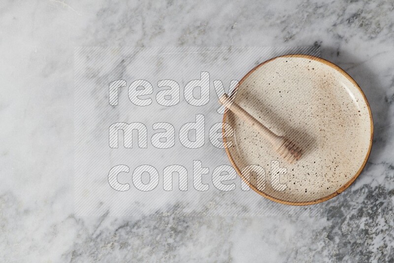 Beige pottery plate with wooden honey dipper in it on grey marble background