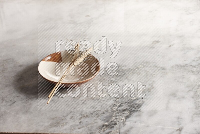 Wheat stalks on multicolored pottery plate on grey marble background
