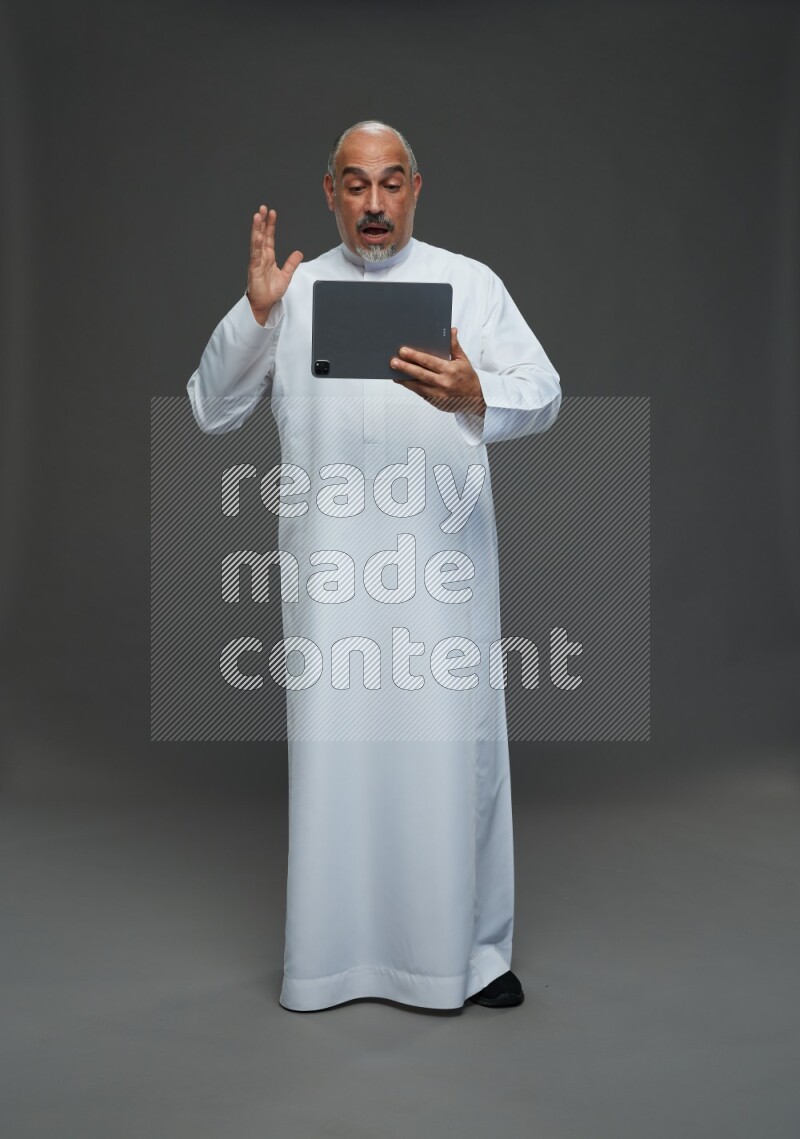 Saudi man without shomag Standing working on tablet on gray background