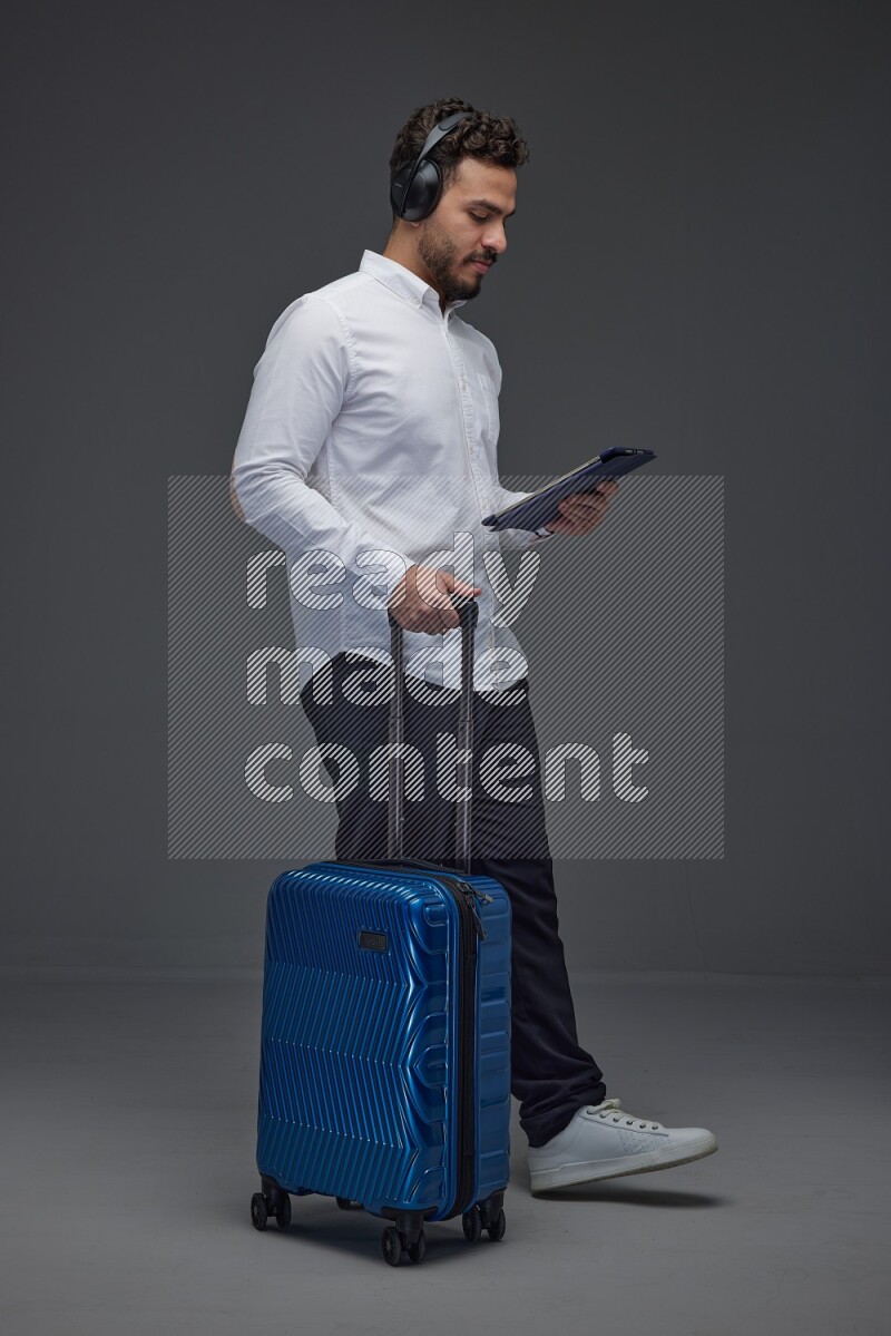 A man wearing smart casual with and pulling a carry-on luggage eye level on a gray background