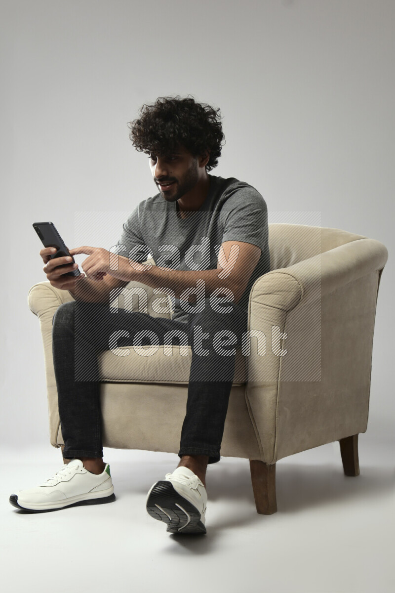 A man wearing casual sitting on a chair browsing on the phone on white background