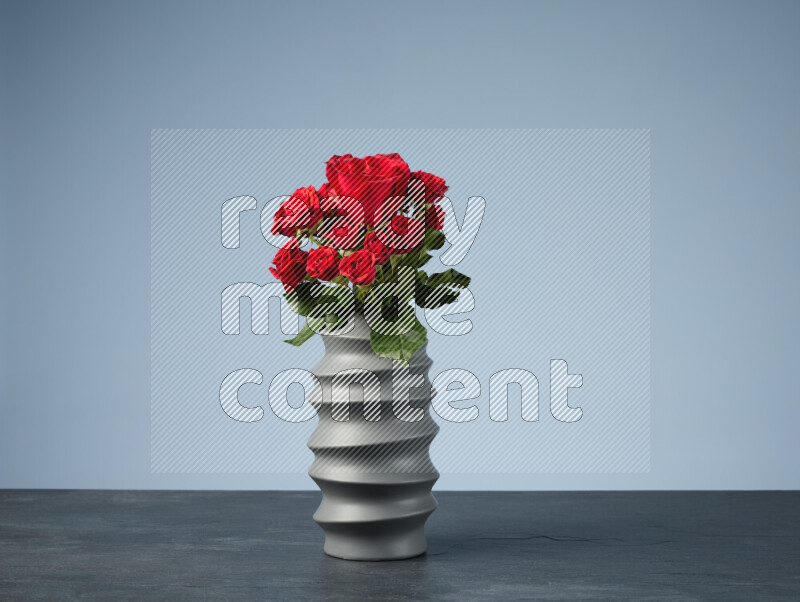 An arrangement of vivid red roses in a grey spiral vase on black marble background