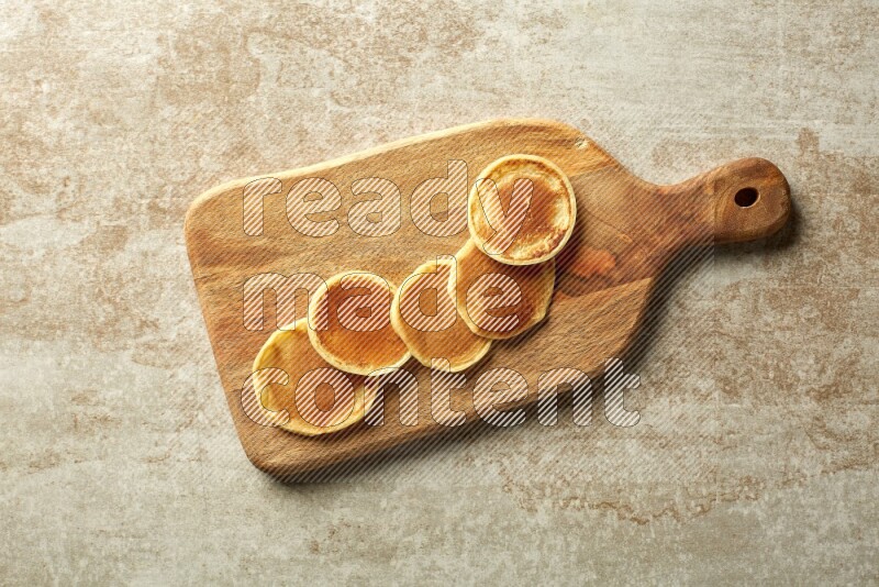 Five stacked plain mini pancakes on a wooden board on beige background
