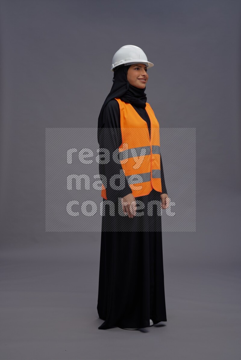 Saudi woman wearing Abaya with engineer vest standing interacting with the camera on gray background