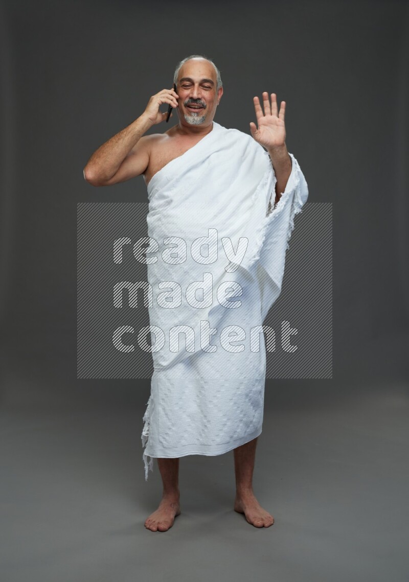A man wearing Ehram Standing talking on phone on gray background