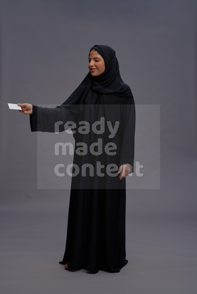 Saudi woman wearing Abaya standing holding ATM card on gray background