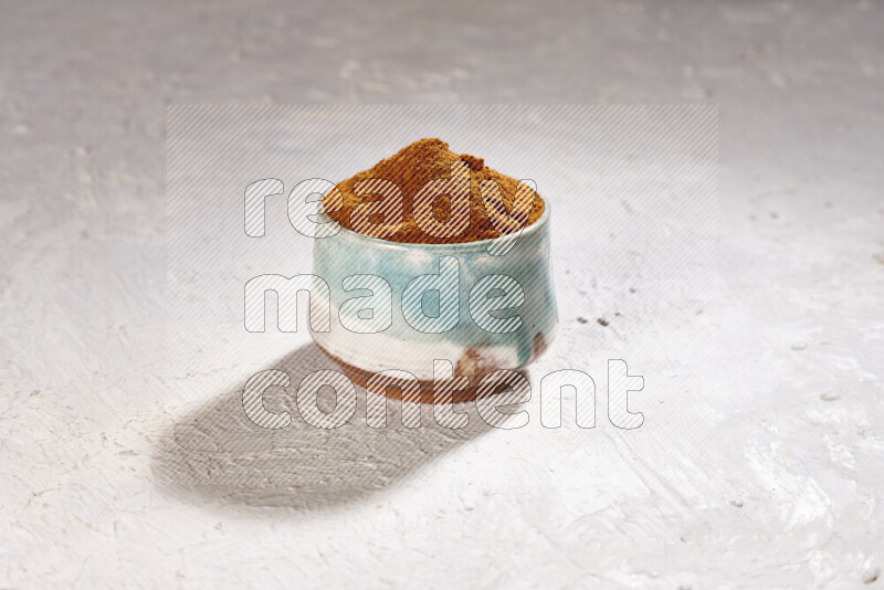 A colored pottery bowl full of ground paprika powder on white background