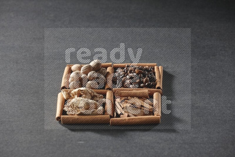 4 مربعات من عيدان القرفة ممتلئة بحبوب القهوة وقطع القرفة والزجبيل المجفف وجوزة الطيب على أرضية سوداء