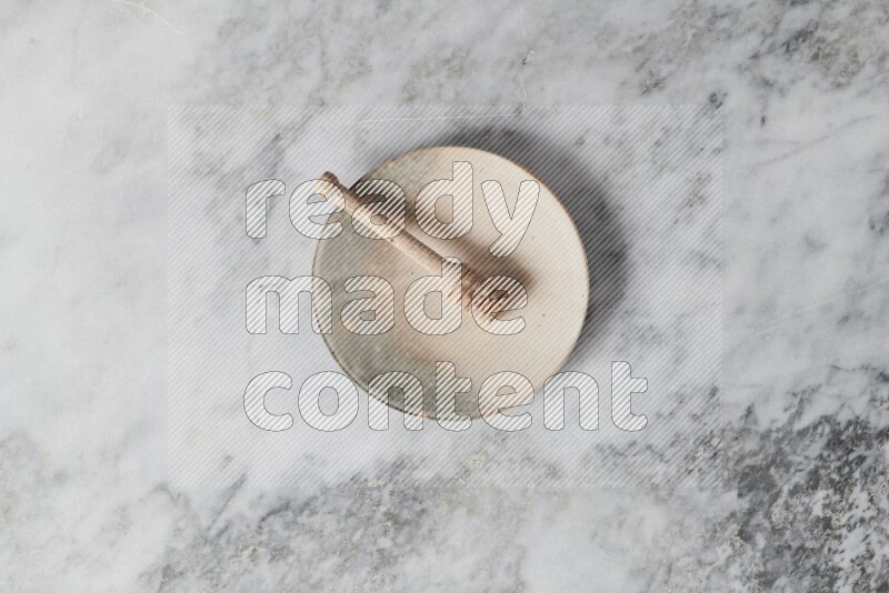 Multicolored pottery plate with wooden honey dipper in it on grey marble background